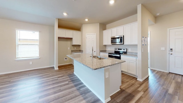 kitchen with light stone counters, a center island with sink, stainless steel appliances, and white cabinetry