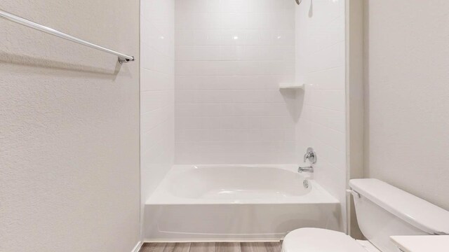 bathroom with hardwood / wood-style floors, tiled shower / bath combo, and toilet