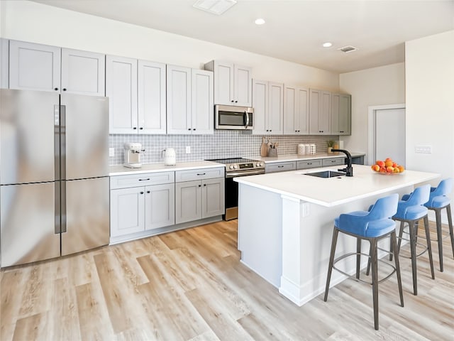 kitchen featuring a kitchen bar, light hardwood / wood-style floors, stainless steel appliances, decorative backsplash, and sink