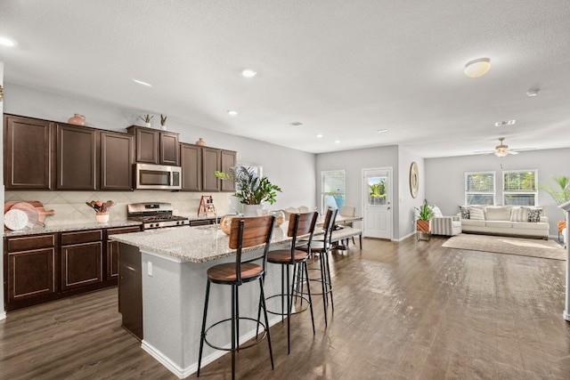 kitchen featuring tasteful backsplash, a center island with sink, dark wood-type flooring, appliances with stainless steel finishes, and a breakfast bar