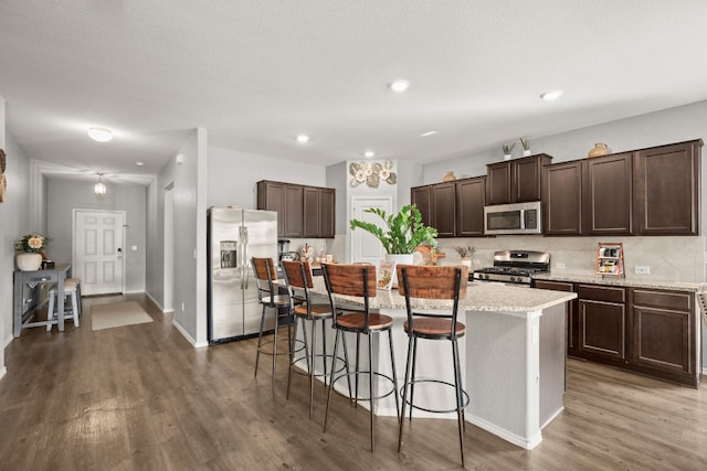 kitchen with a kitchen island, a breakfast bar area, stainless steel appliances, dark brown cabinetry, and dark hardwood / wood-style floors