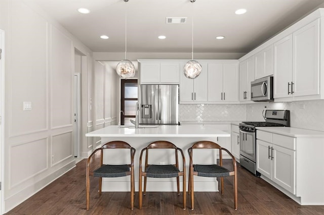 kitchen with pendant lighting, a kitchen island with sink, dark wood-type flooring, white cabinets, and stainless steel appliances