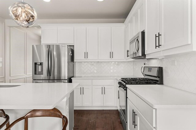 kitchen featuring appliances with stainless steel finishes, white cabinets, pendant lighting, a kitchen bar, and dark hardwood / wood-style floors