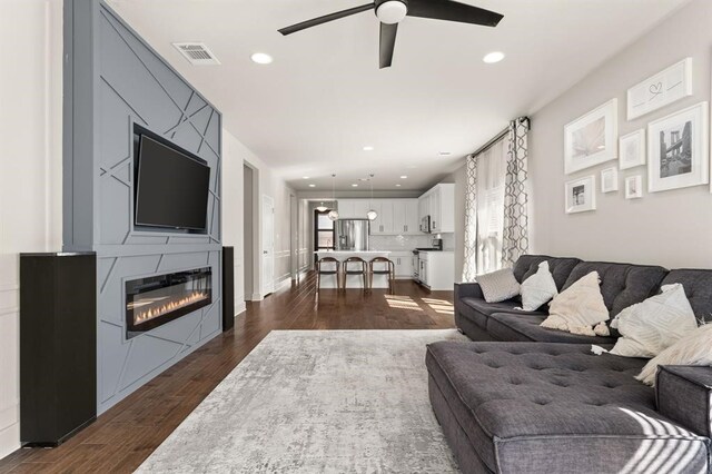 living room featuring ceiling fan, a fireplace, and dark hardwood / wood-style floors