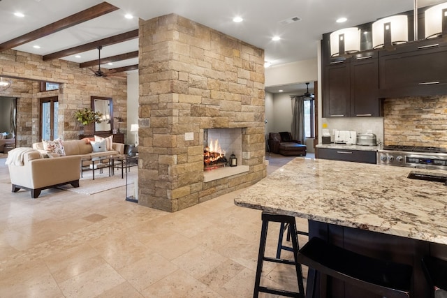 kitchen featuring dark brown cabinetry, decorative light fixtures, a fireplace, a breakfast bar area, and light stone countertops