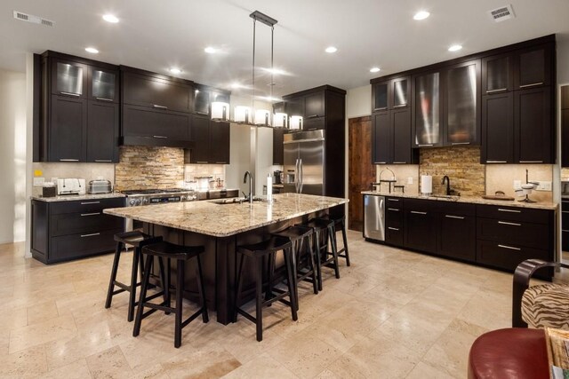 kitchen with an island with sink, stainless steel appliances, pendant lighting, and sink