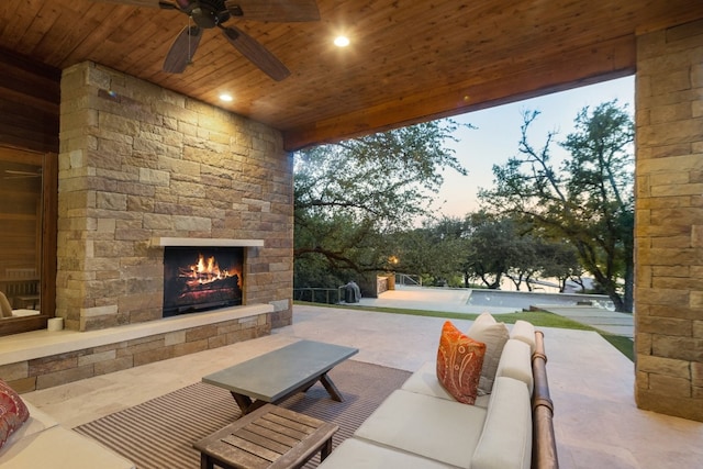 patio terrace at dusk with ceiling fan and an outdoor stone fireplace