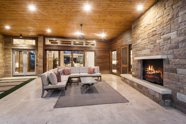 living room with wood ceiling, wood walls, a stone fireplace, ceiling fan, and french doors