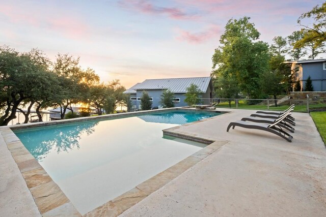 pool at dusk featuring a patio area and a diving board