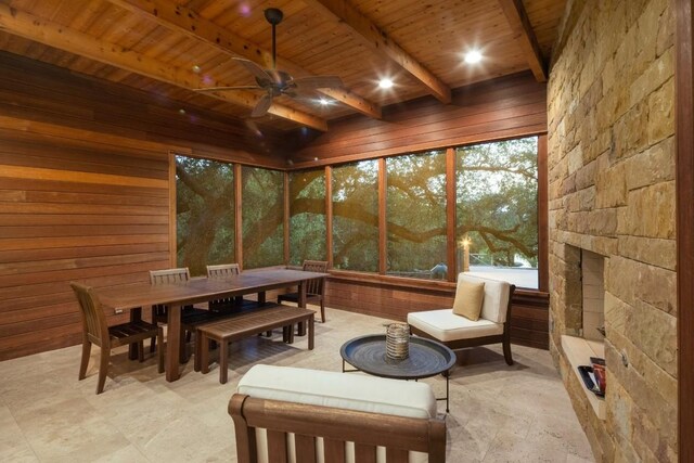 sunroom with wood ceiling, ceiling fan, beamed ceiling, and a stone fireplace