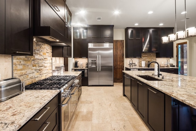 kitchen featuring pendant lighting, sink, tasteful backsplash, premium appliances, and light stone countertops