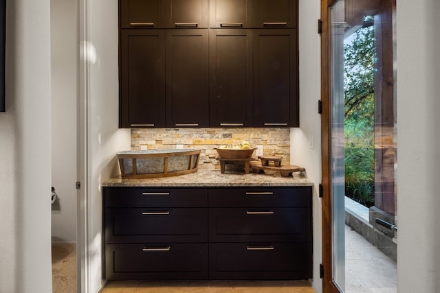 bar with dark brown cabinets, light stone countertops, and decorative backsplash