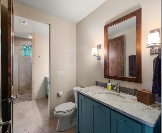 bathroom featuring a tile shower, vanity, and toilet