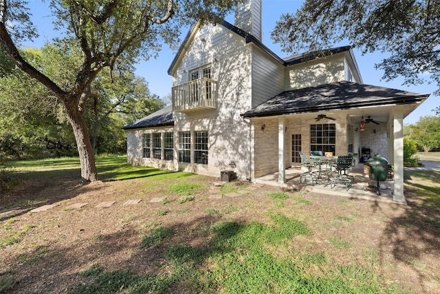 rear view of house featuring ceiling fan, a balcony, a lawn, and a patio