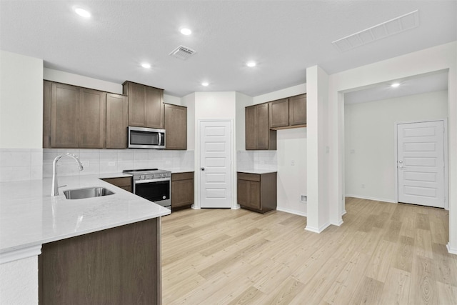 kitchen with sink, dark brown cabinetry, light wood-type flooring, appliances with stainless steel finishes, and tasteful backsplash