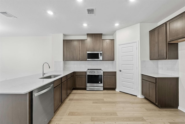 1721 Tin Can Trl, Georgetown, TX 78628 - kitchen featuring appliances with stainless steel finishes, a sink, light wood-style floors, a peninsula, and decorative backsplash
