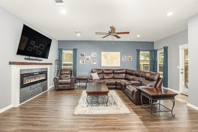 living room with ceiling fan, wood-type flooring, a wealth of natural light, and a tiled fireplace