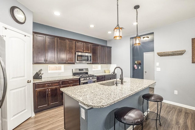 kitchen featuring tasteful backsplash, light hardwood / wood-style flooring, decorative light fixtures, a center island with sink, and appliances with stainless steel finishes