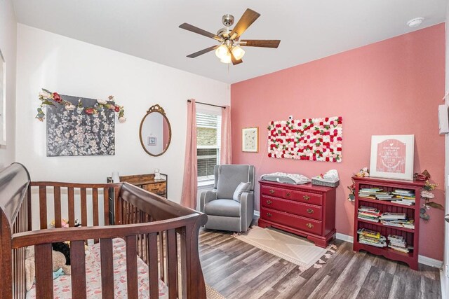 bedroom with dark hardwood / wood-style floors, a nursery area, and ceiling fan