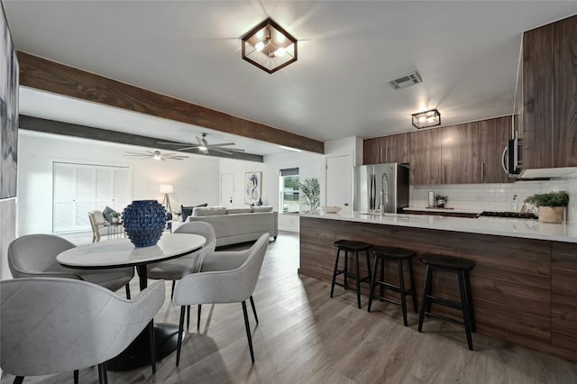 dining space featuring ceiling fan, beam ceiling, and light wood-type flooring