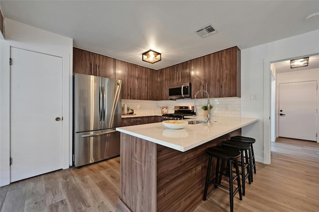 kitchen featuring stainless steel appliances, backsplash, sink, a breakfast bar, and light hardwood / wood-style flooring