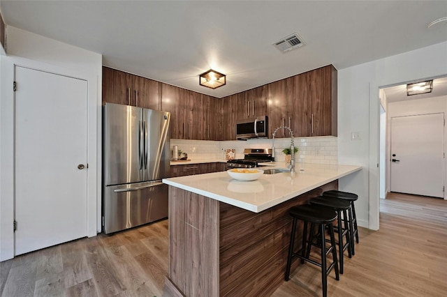 1130 Gardner Rd, Austin, TX 78721 - kitchen featuring stainless steel appliances, a peninsula, a kitchen breakfast bar, light countertops, and decorative backsplash