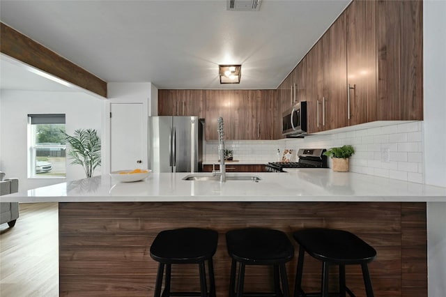 kitchen with stainless steel appliances, decorative backsplash, light hardwood / wood-style floors, a kitchen breakfast bar, and kitchen peninsula