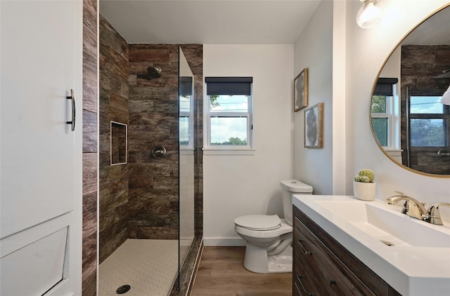 bathroom with hardwood / wood-style floors, vanity, toilet, and tiled shower