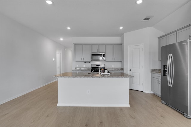 kitchen featuring lofted ceiling, light stone countertops, a kitchen island with sink, and appliances with stainless steel finishes