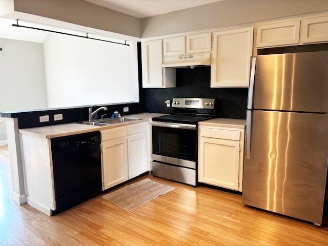 5608 Cougar Dr Unit 219, Austin, TX 78745 - kitchen with appliances with stainless steel finishes, under cabinet range hood, a sink, light wood finished floors, and decorative backsplash