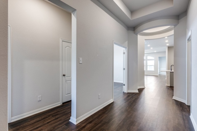 corridor with sink, a tray ceiling, and dark hardwood / wood-style flooring