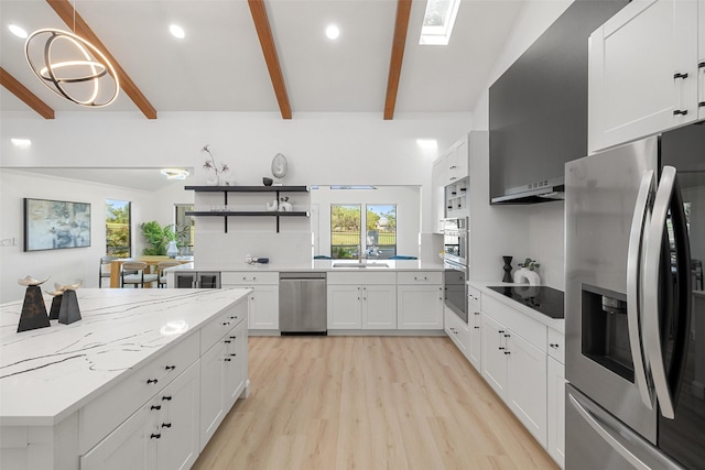 kitchen with vaulted ceiling with skylight, light hardwood / wood-style floors, white cabinetry, light stone countertops, and stainless steel appliances