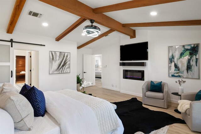 bedroom with light wood-type flooring, ensuite bathroom, a barn door, and lofted ceiling with beams