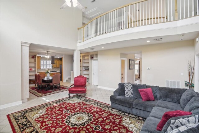 living room featuring built in shelves, ceiling fan, a towering ceiling, and light tile patterned flooring