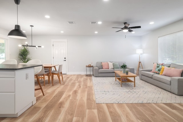 living room with ceiling fan with notable chandelier and light hardwood / wood-style floors