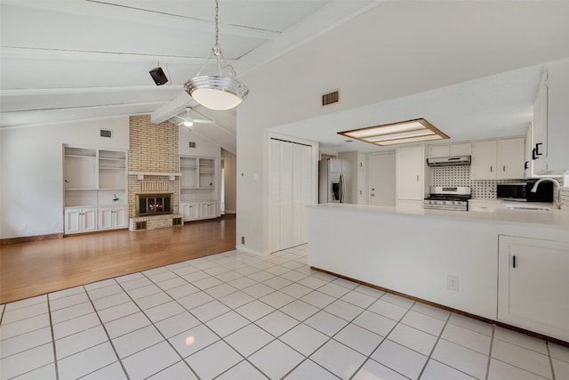 kitchen with a brick fireplace, white cabinets, pendant lighting, stainless steel appliances, and light hardwood / wood-style flooring