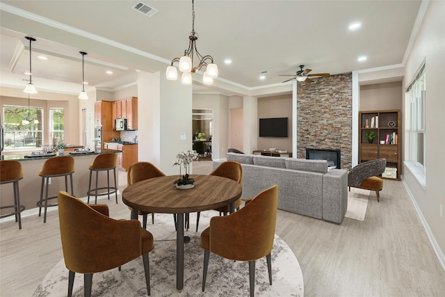 dining room featuring a fireplace, ceiling fan with notable chandelier, light hardwood / wood-style flooring, and crown molding