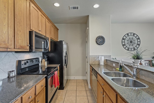 kitchen featuring dark stone counters, sink, backsplash, appliances with stainless steel finishes, and light tile patterned floors