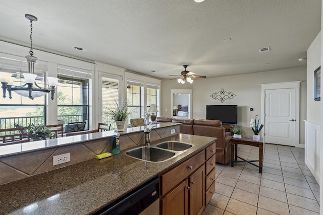 kitchen with ceiling fan with notable chandelier, pendant lighting, a textured ceiling, dark stone counters, and sink