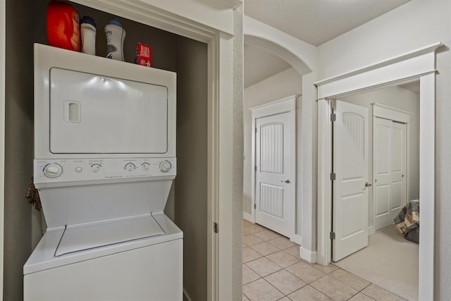 laundry room with light tile patterned flooring, a textured ceiling, and stacked washing maching and dryer