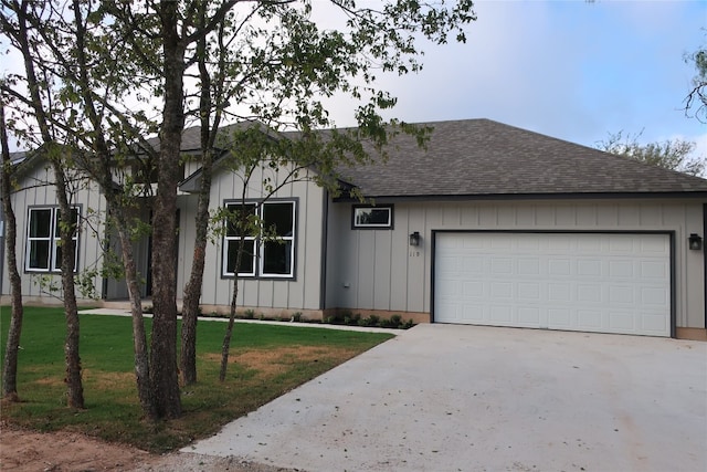 view of front of home featuring board and batten siding, a front lawn, roof with shingles, driveway, and an attached garage