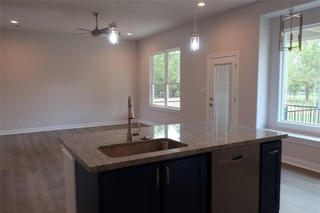 kitchen featuring light stone counters, a kitchen island with sink, sink, hanging light fixtures, and stainless steel dishwasher