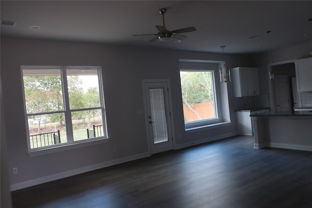 unfurnished living room with ceiling fan, dark wood-type flooring, and a healthy amount of sunlight