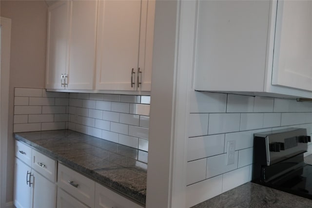 kitchen featuring backsplash, dark stone countertops, and white cabinets