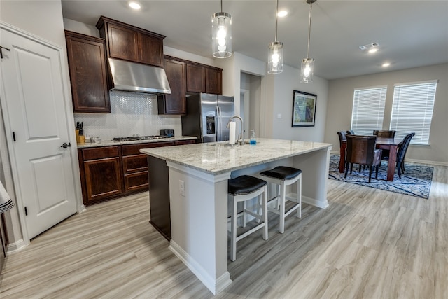 kitchen featuring decorative light fixtures, a kitchen island with sink, ventilation hood, stainless steel appliances, and light hardwood / wood-style floors