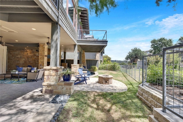 view of yard featuring ceiling fan, a balcony, an outdoor living space with a fire pit, and a patio area