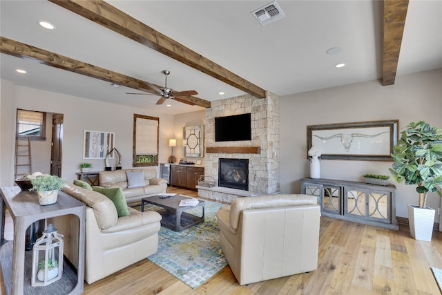 living room featuring light wood-type flooring, a fireplace, ceiling fan, and beamed ceiling