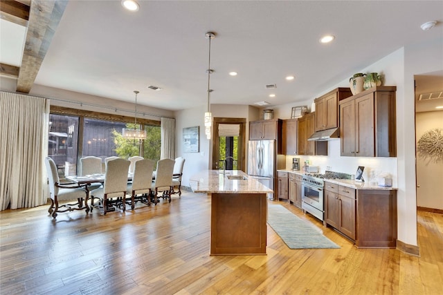 kitchen with pendant lighting, stainless steel appliances, beam ceiling, light hardwood / wood-style flooring, and a center island with sink