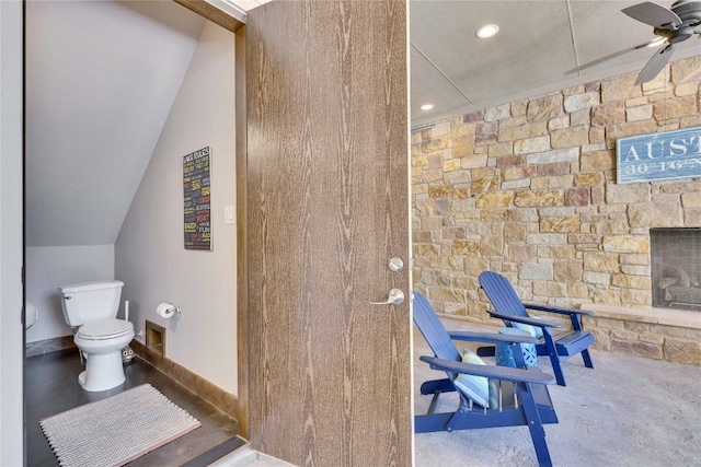 interior space with ceiling fan, a stone fireplace, toilet, and concrete floors