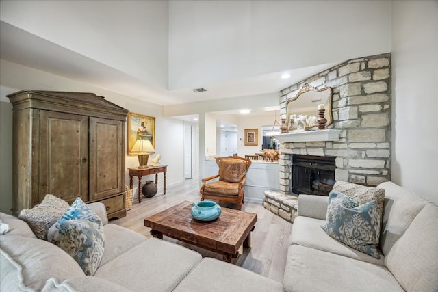 living room with a stone fireplace, a high ceiling, and light wood-type flooring